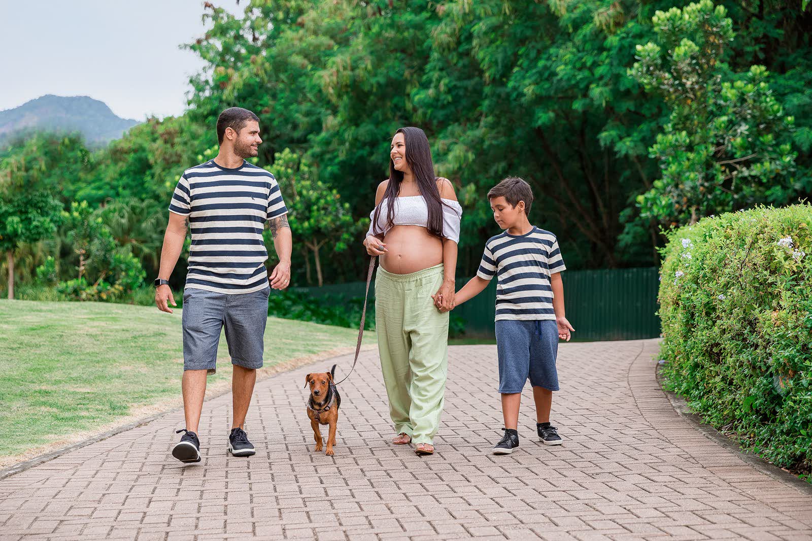 Gestante caminhando ao ar livre de mãos dadas com o filho e o companheiro, ilustrando o período de afastamento do trabalho