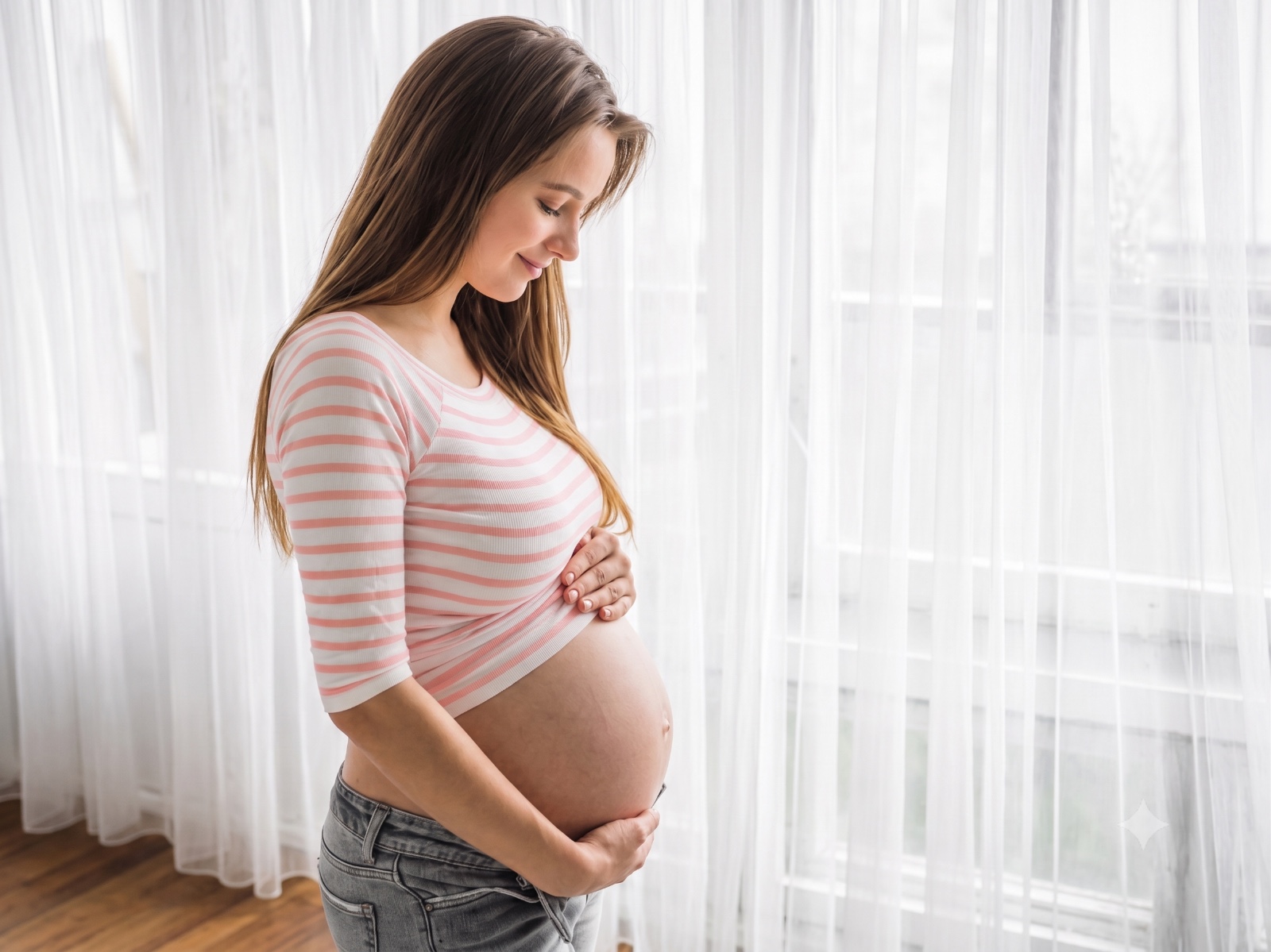 Mulher grávida em pé, com as duas mãos na barriga, em ambiente interno iluminado